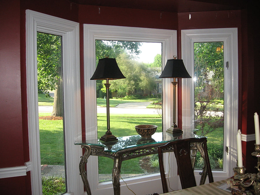 A bare bay window in a dining room, with a console table and lamps and no window treatment