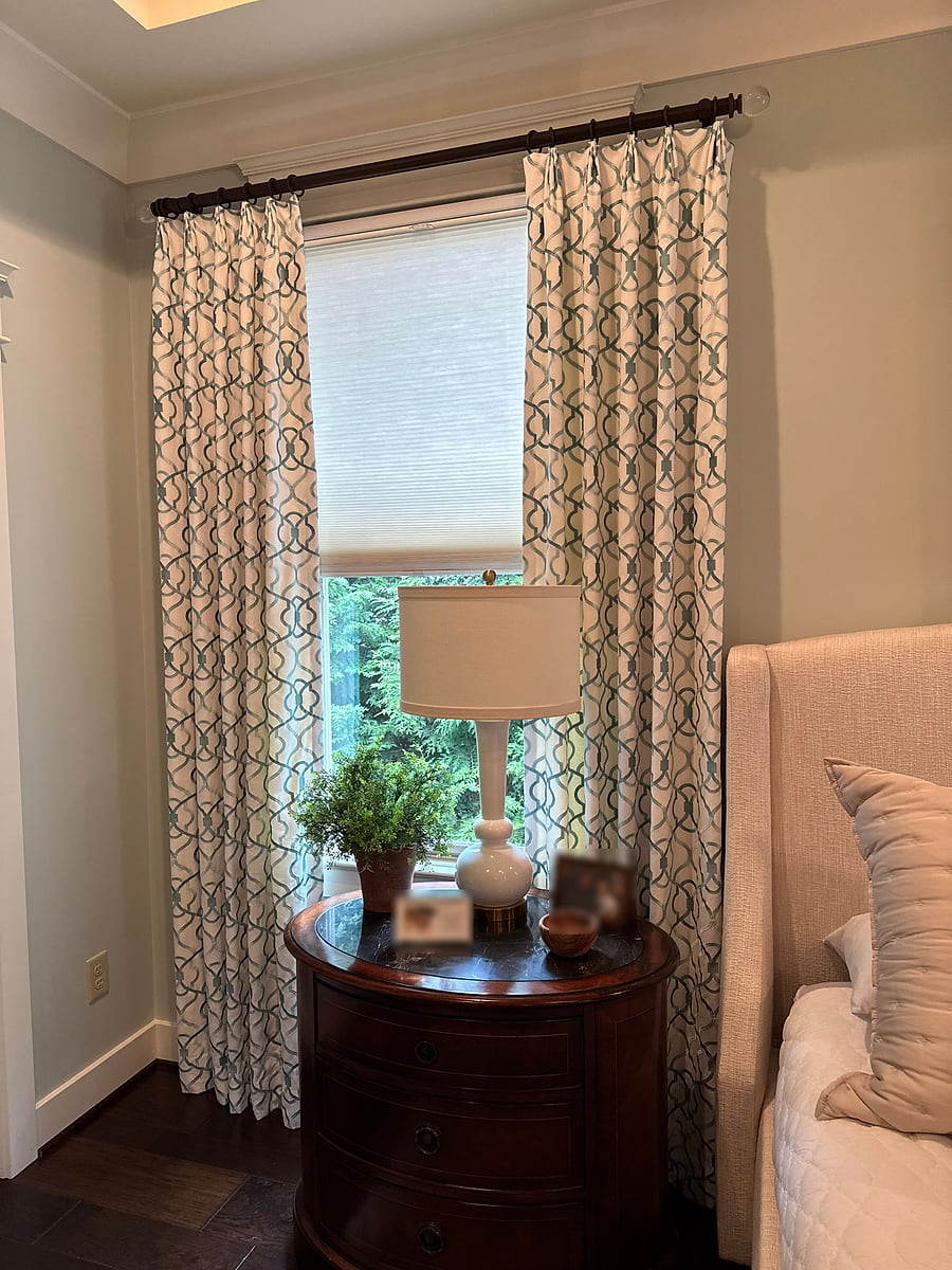 A bedroom corner with patterned floor-length drapes, a lamp and a nightstand