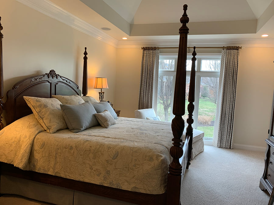 A bedroom with a four-poster bed and full-length draperies at the window