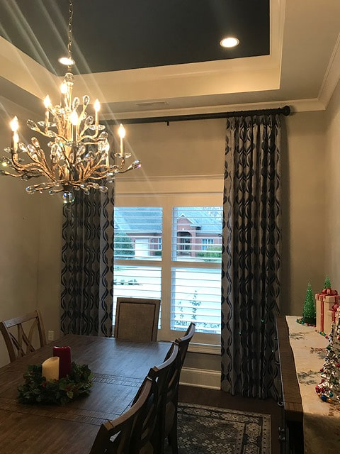 A dining room with patterned floor-length drapes, a tray ceiling and a chandelier