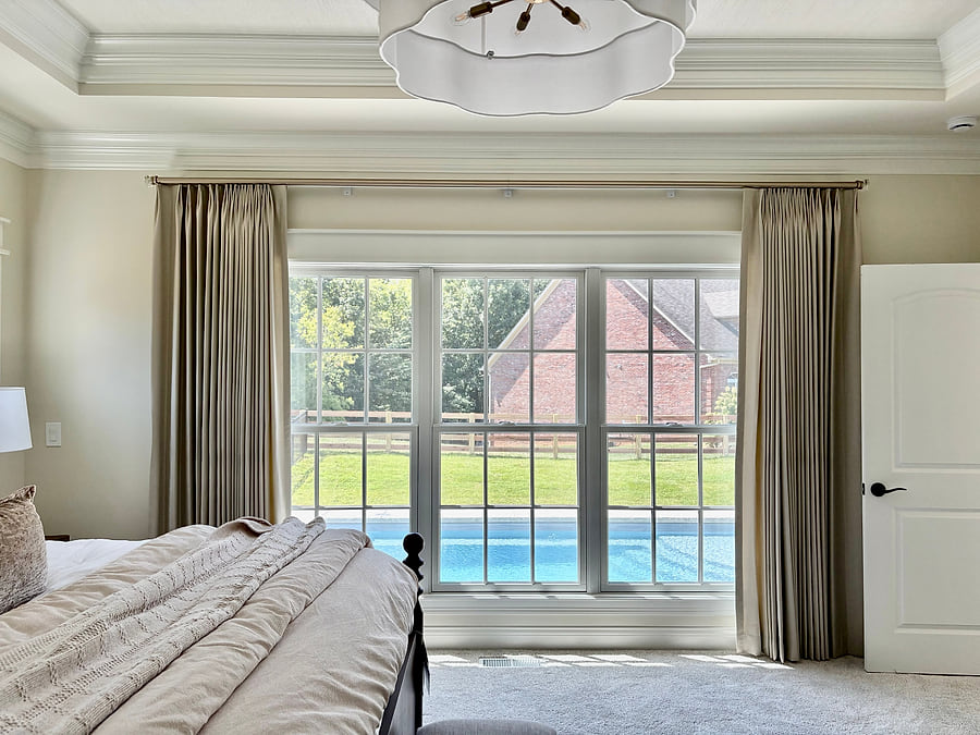 A main bedroom with full-length drapes framing a window that looks onto a pool