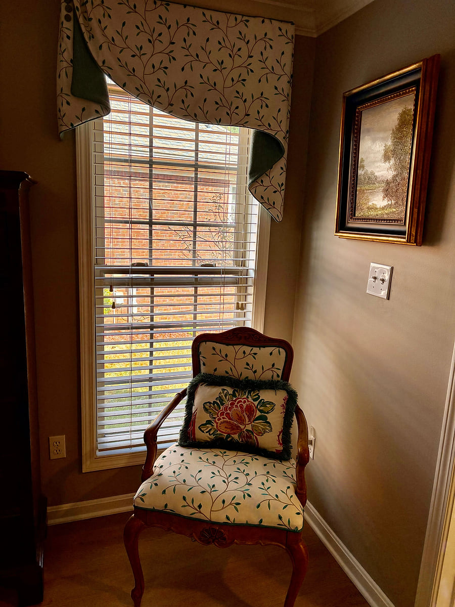 A chair reupholstered in a floral fabric, beside a shuttered window