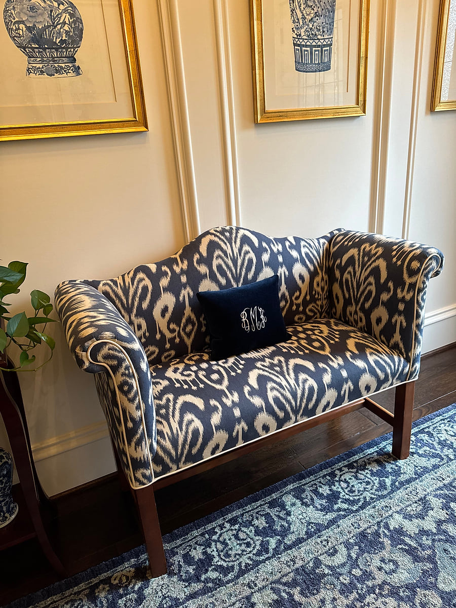 A settee reupholstered in a blue and cream patterned fabric, against a panelled wall
