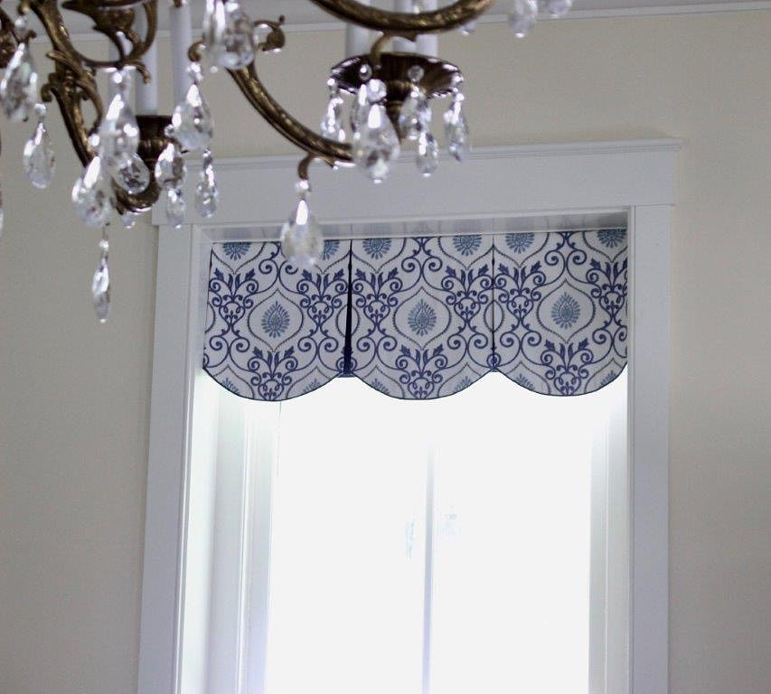 A patterned valance with red trim over shuttered windows