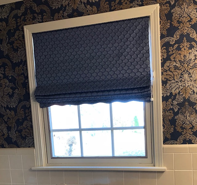 A navy patterned roman shade against matching wallpaper