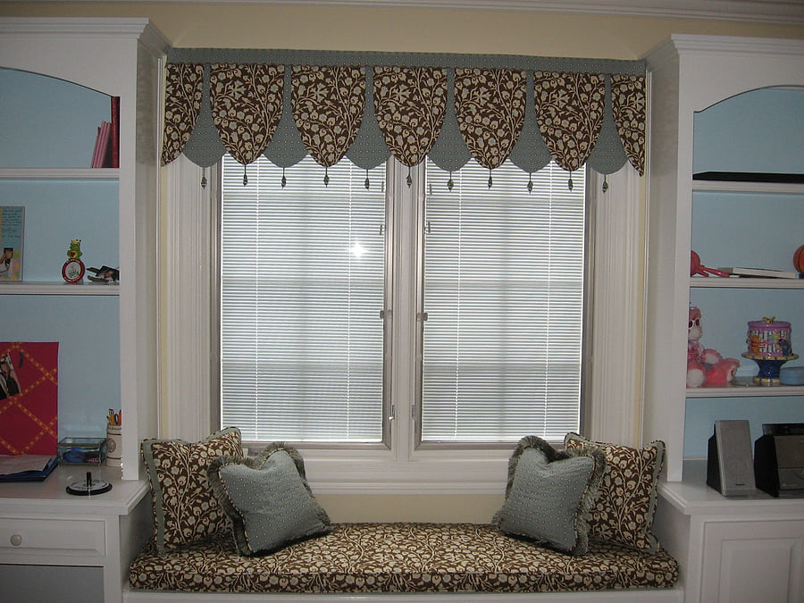 A child's room with a patterned scalloped valance and a cushioned window seat