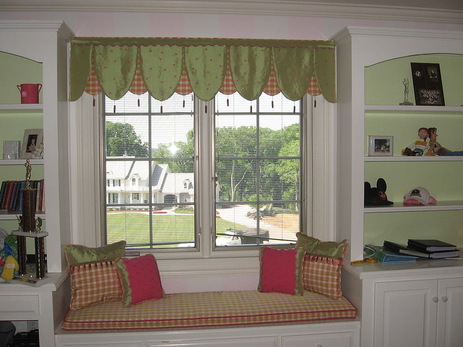 A child's room with a green scalloped valance and a window seat in checked fabric